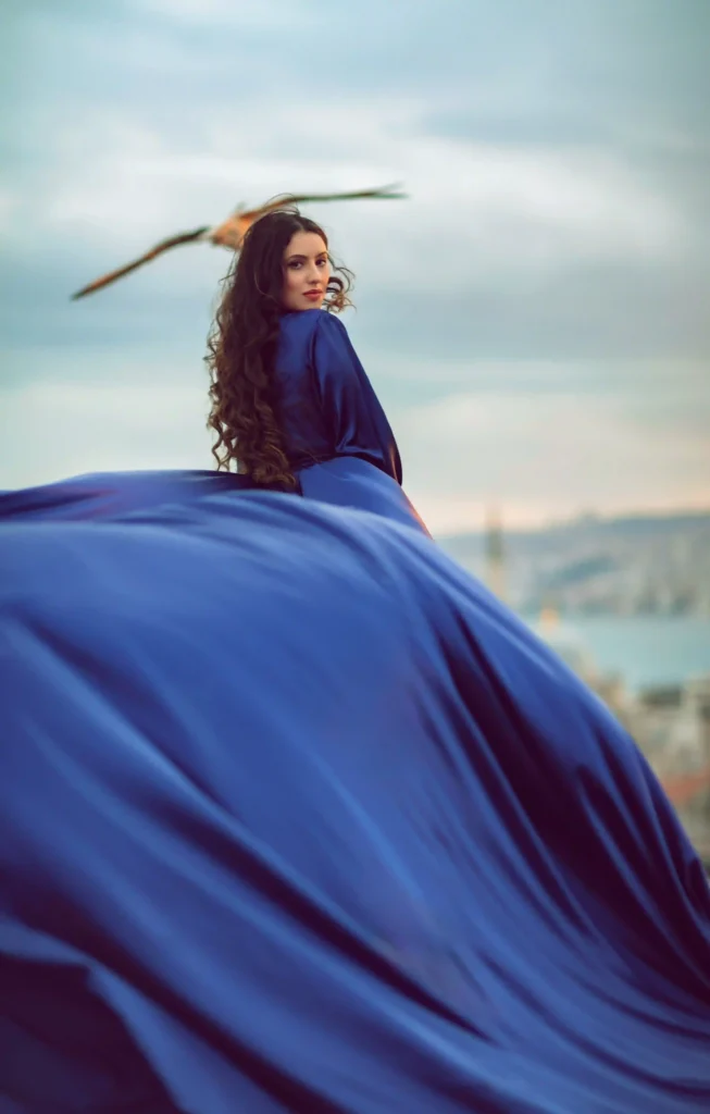 Luxury rooftop photoshoot in Istanbul with a woman wearing a flowing blue dress, a flying bird above her, and panoramic Bosphorus views.