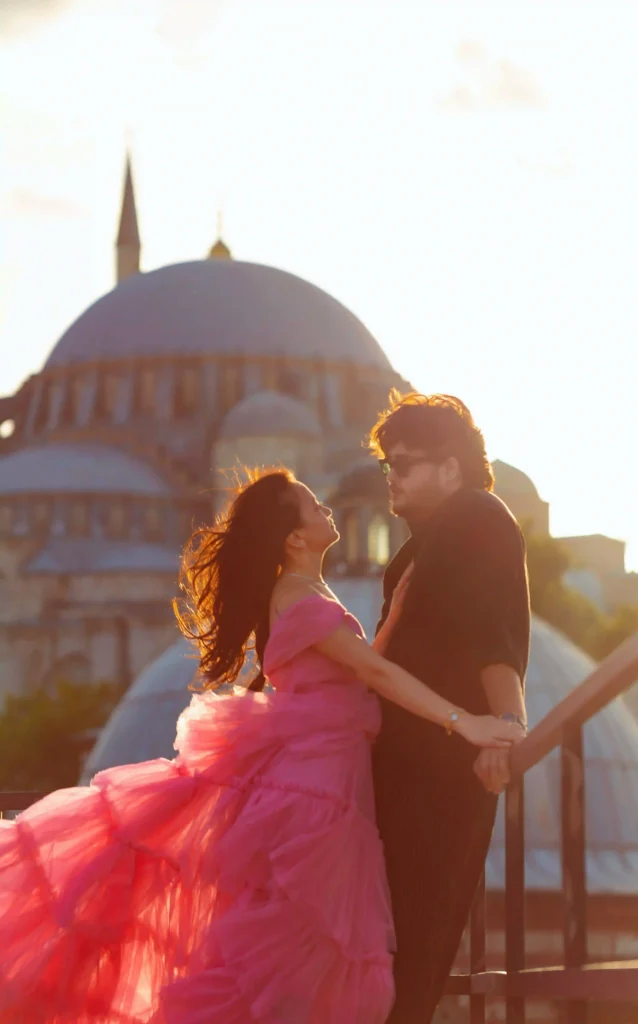 Romantic couple rooftop photoshoot in Istanbul with a flowing pink flying dress and the iconic Süleymaniye Mosque glowing in the golden sunset.
